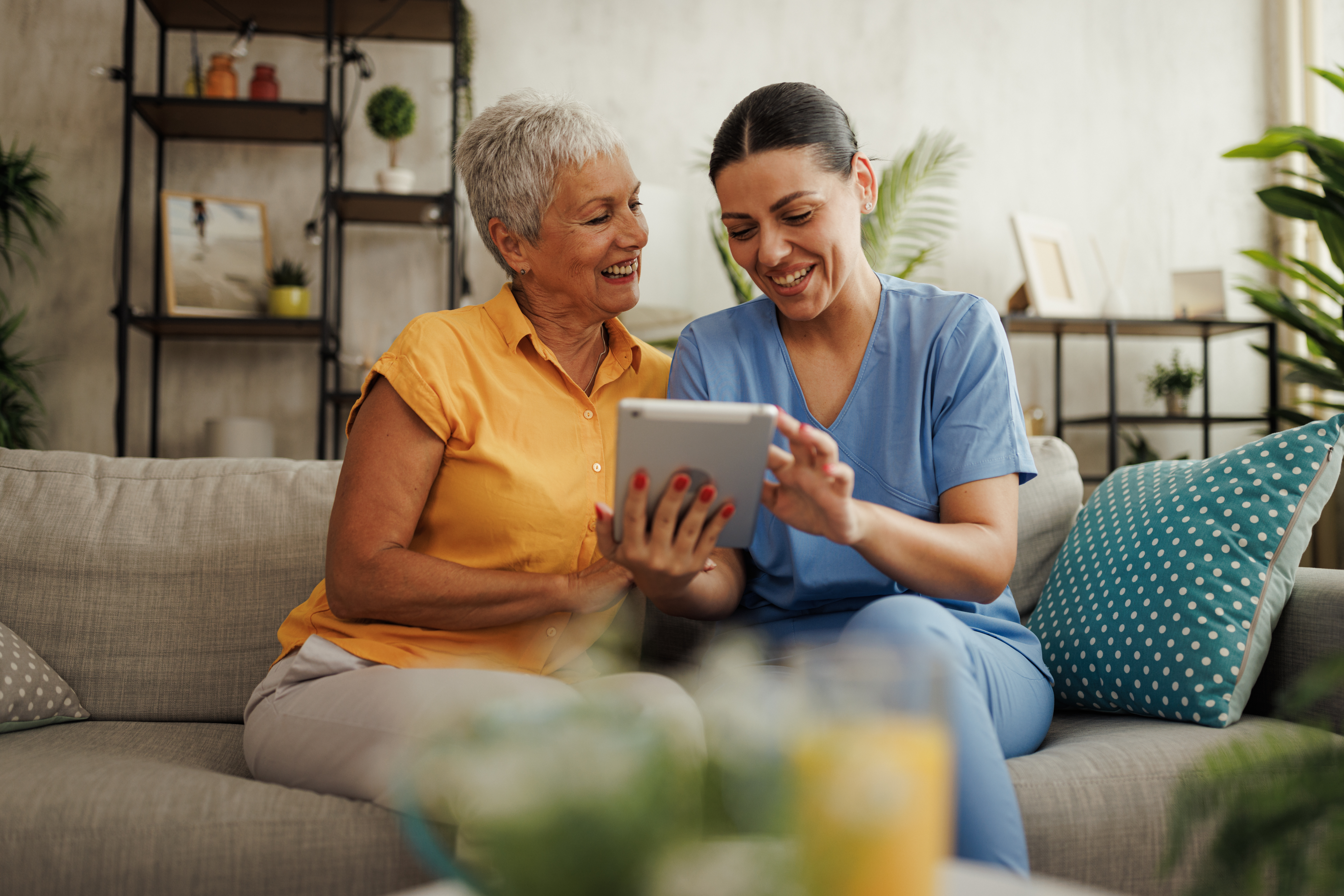 A caregiver and an elderly resident smiling at a tablet together